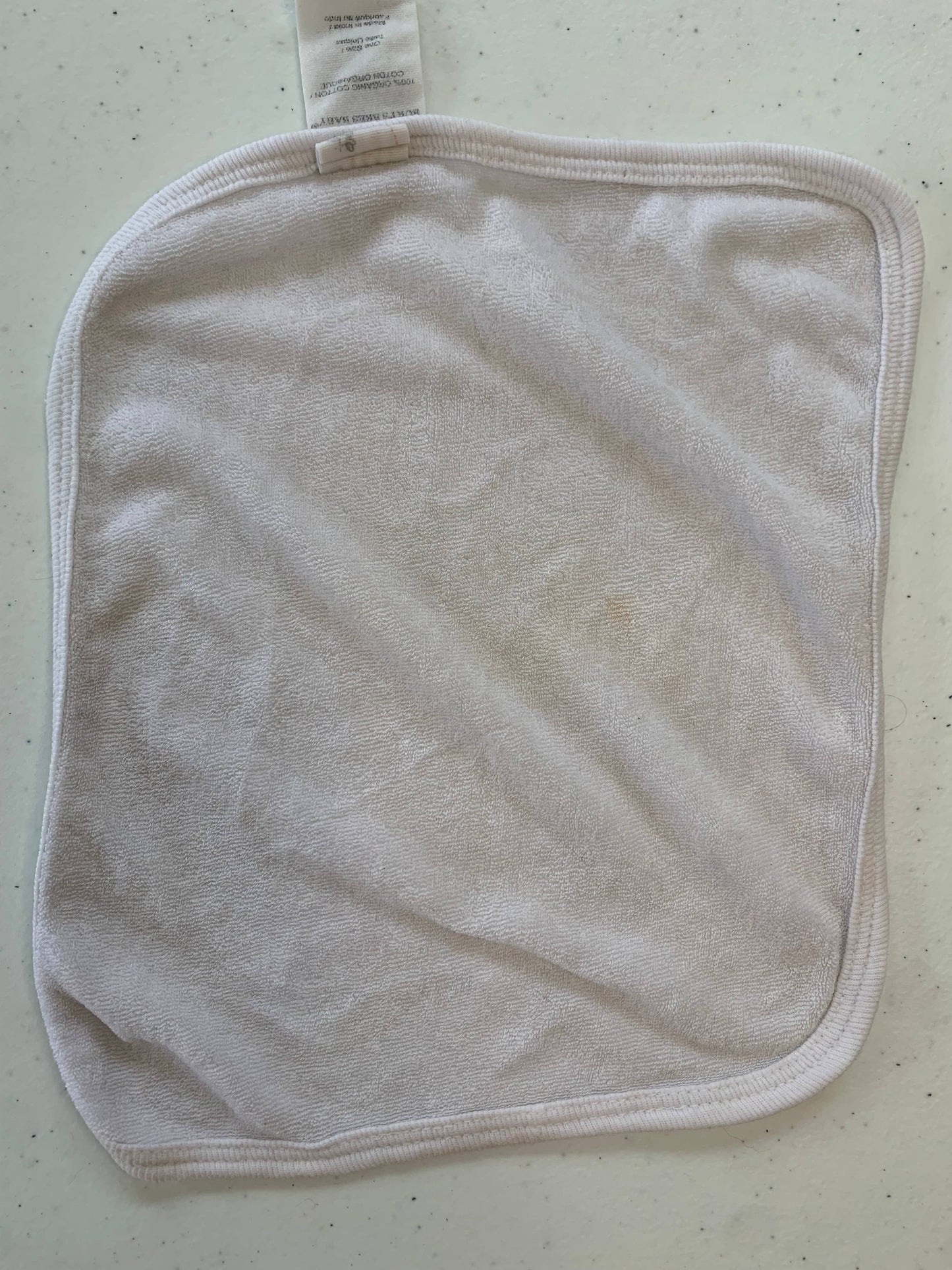White natural cotton baby washcloth with tag on cream surface, soft fabric for gentle cleansing
