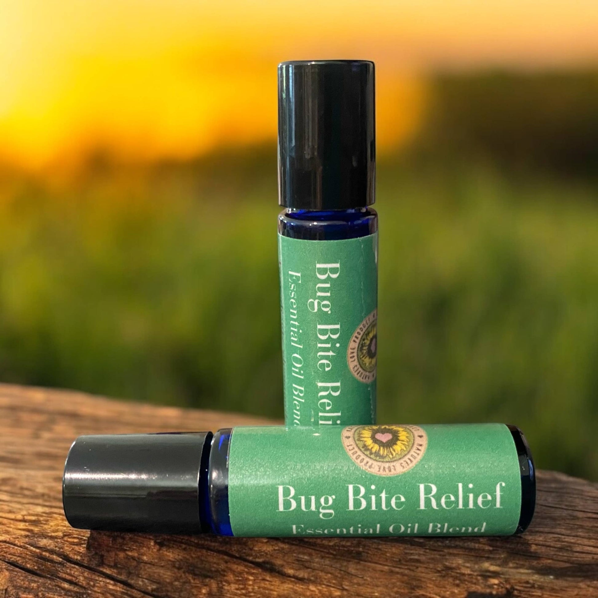 Two bottles of Bug Bite Relief essential oil blend by Rooted In Faith Apothecary on wooden surface at sunset