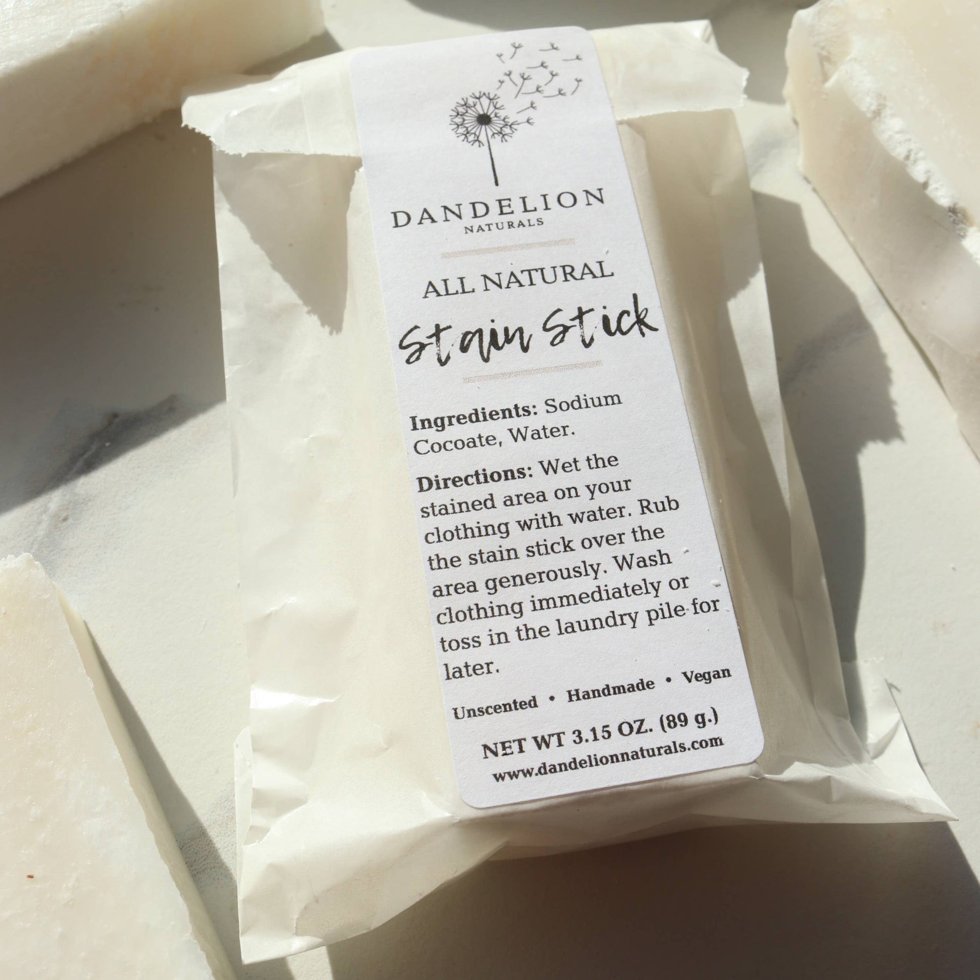 Dandelion Naturals all natural stain stick soap bar wrapped in white paper packaging on light surface