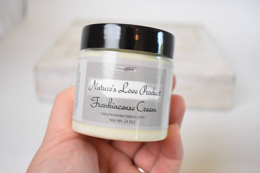 Hand holding a jar of Nature's Love Product frankincense cream with black lid on a white background