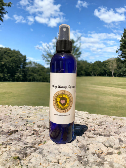 Blue spray bottle of Bug Away Spray by Nature's Love on a stone surface with grassy field and blue sky background
